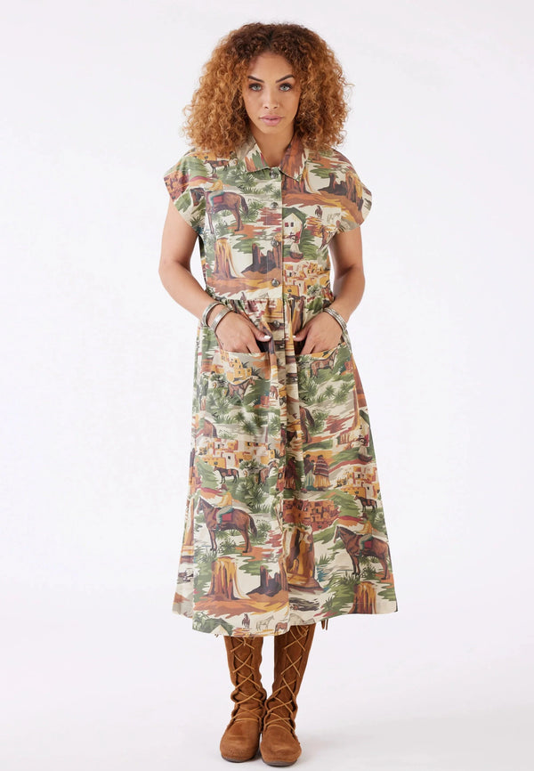 Woman wearing a dress that depicts a scene of Native American women walking through the valley in the most beautiful earthy colors. Plus it's got handy patch pockets on the pleated skirt