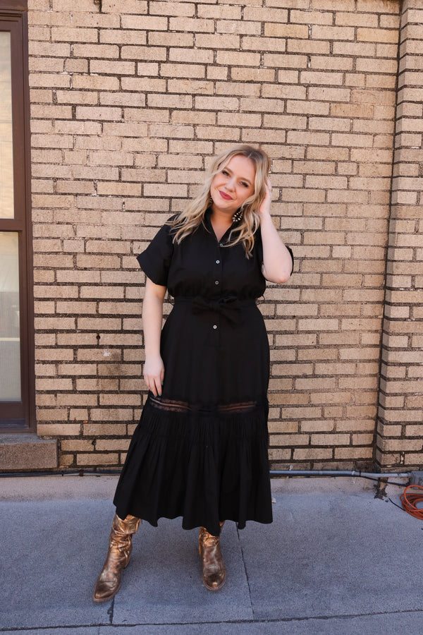 Woman wearing black midi button front dress features a flattering cinched waist, elegant collar with lace detail, and short sleeves. Complete the look with the matching belt.
