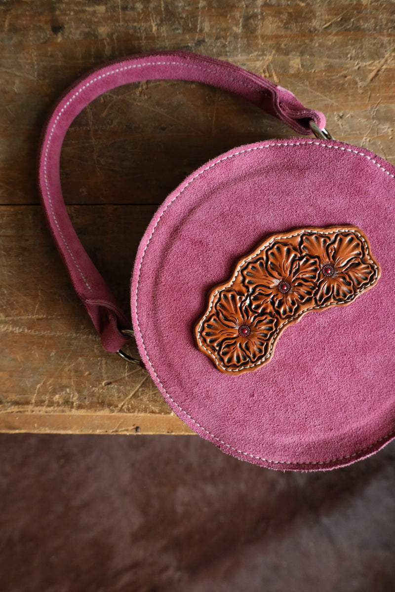 Purse crafted from mauve roughout leather, this purse features a beautiful circle design with a floral tooled front. Its matching handle and zipper closure provide convenience, while the twin interior pockets offer ample storage.