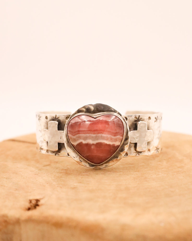 Distinctive hammered finish cuff, featuring two sterling silver crosses and a 3D rhodochrosite heart at its center