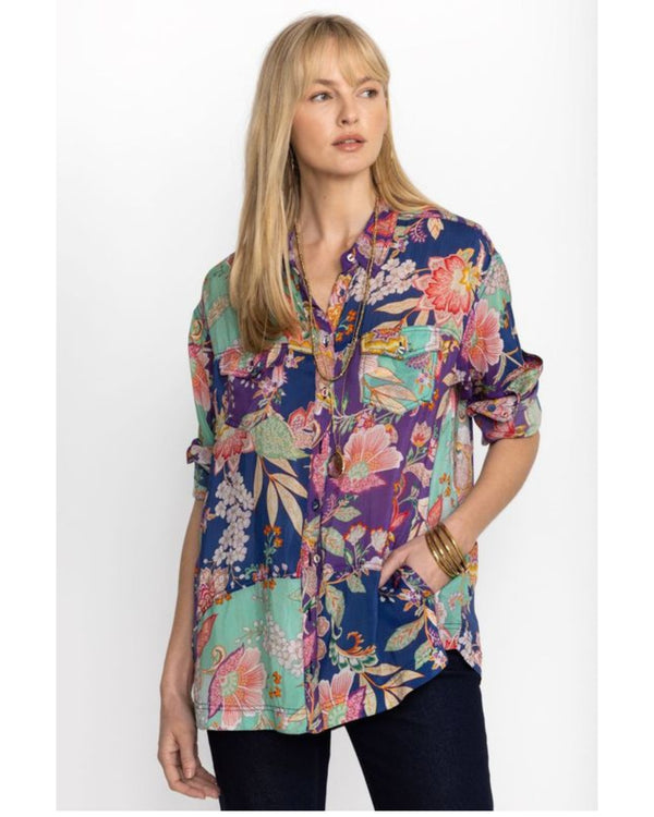 Woman wearing button up long sleeve blouse with blue, green and purple patchwork on it with multicolor flowers throughout 