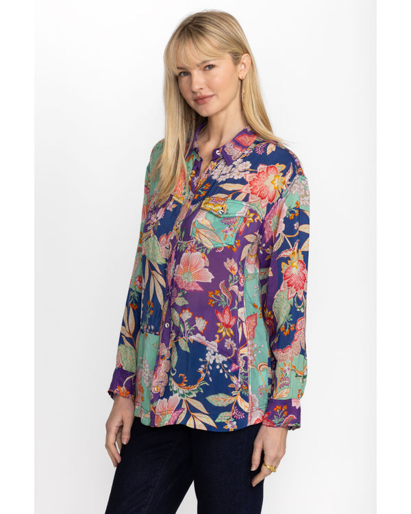 Woman wearing button up long sleeve blouse with blue, green and purple patchwork on it with multicolor flowers throughout