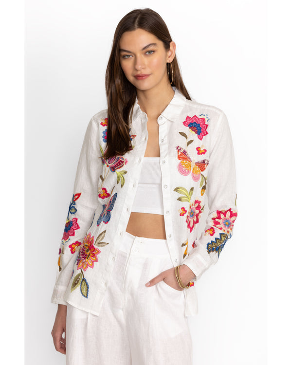 Woman wearing white button down linen blouse with multicolor flowers and butterflies embroidered throughout 