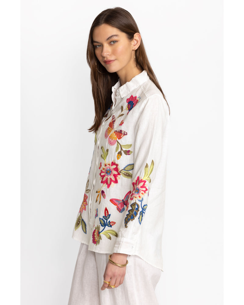 Woman wearing white button down linen blouse with multicolor flowers and butterflies embroidered throughout