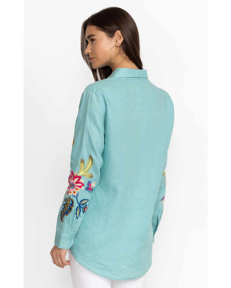 Woman wearing bright blue button up blouse with multicolor flowers and butterflies embroidered throughout