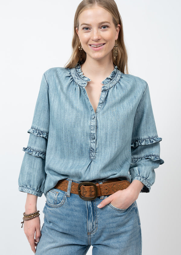 Woman wearing denim top with ruffle accents and button front closure