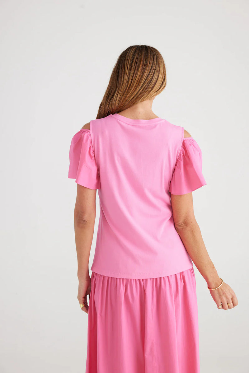 Woman wearing pink top with puff sleeves that have a cutout on the tops of the shoulders