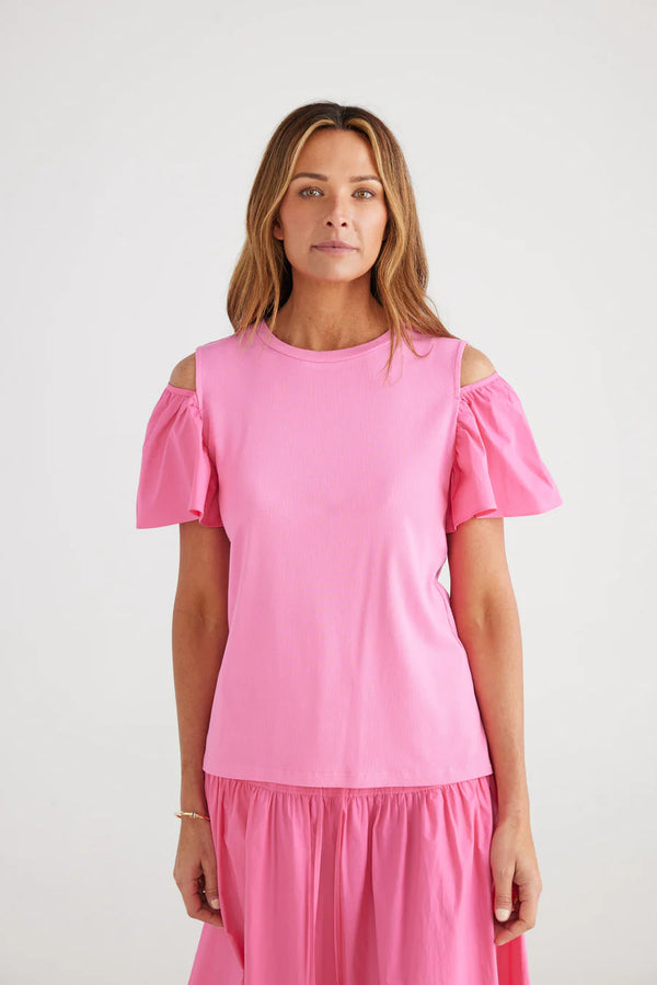 Woman wearing pink top with puff sleeves that have a cutout on the tops of the shoulders