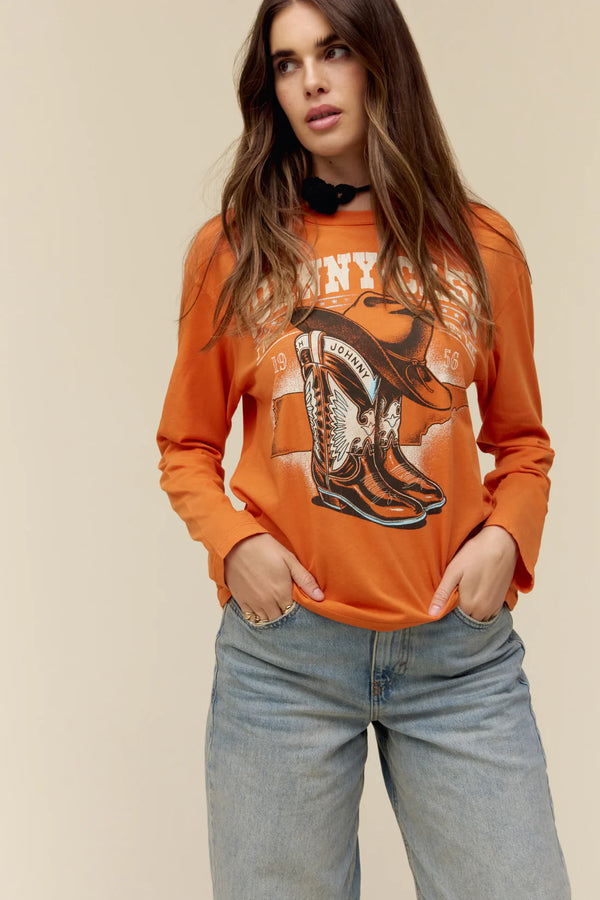 WOMAN WEARING ORANGE LONG SLEEVE TOP WITH PICTURES OF BOOTS AND HAT WITH JOHNNY CASHS NAME