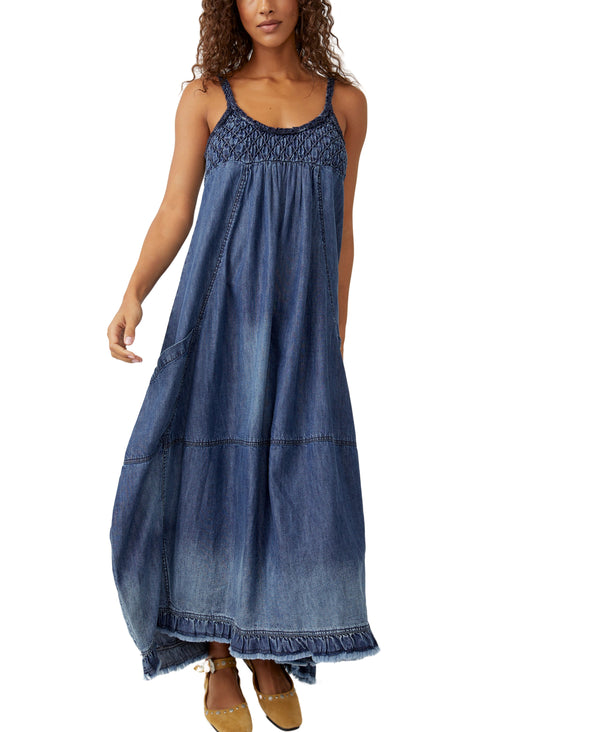 Woman wearing denim spaghetti strap dress with scrunching near the breast region and side pockets. This is a maxi dress