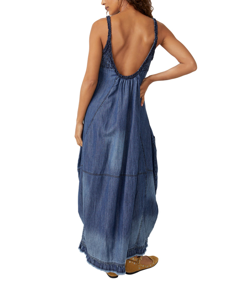 Woman wearing denim spaghetti strap dress with scrunching near the breast region and side pockets. This is a maxi dress