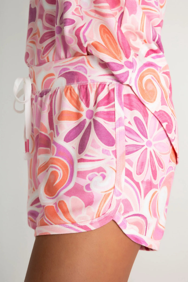 Woman wearing lounge shorts in a pink and orange colorway with floral pattern and paisley print throughout