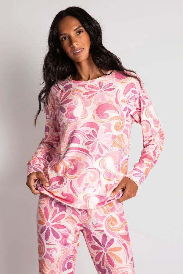 Woman wearing long sleeve lounge top in a pink and orange colorway with floral pattern and paisley print