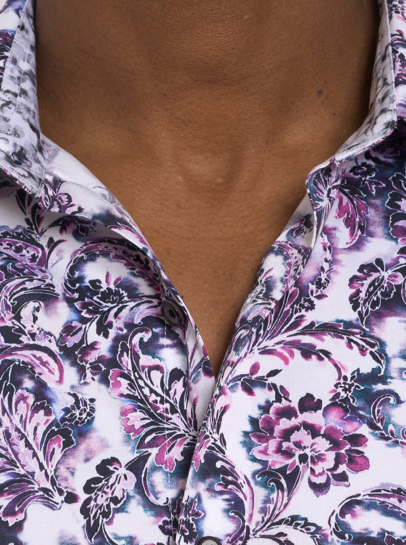 Man wearing long sleeve button down dress shirt with white background with purple, blue and black ornate pattern adorned with floral print all over