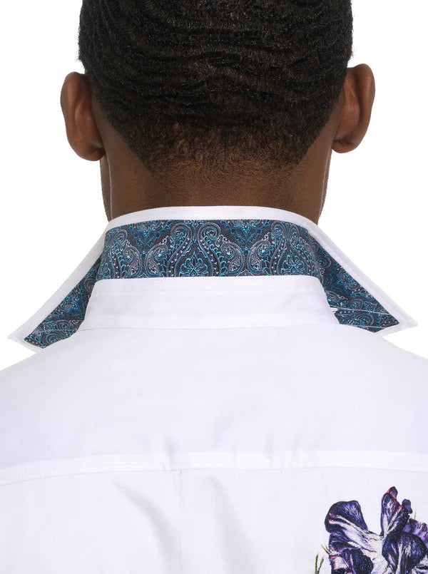Man wearing white button down long sleeve dress shirt with vibrant multicolor floral fappern on back od shirt and into sleeves. On back of shirt, a champagne bottle emerges from floral design
