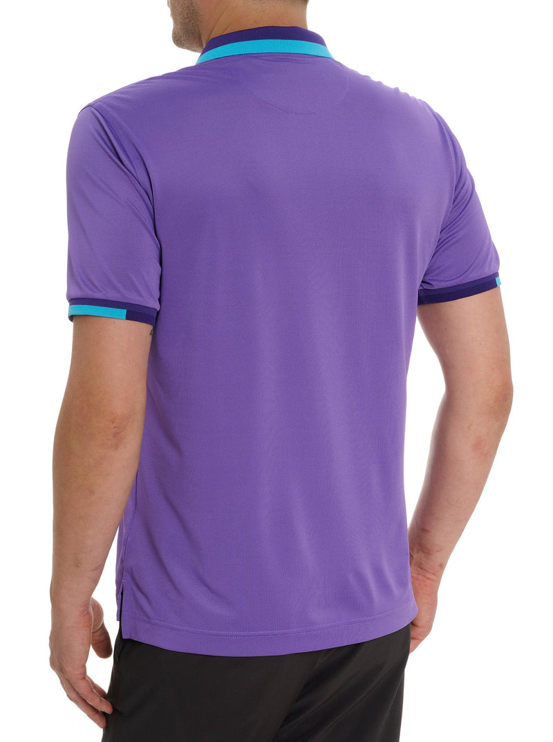 Man wearing purple short sleeve polo with image of embroidered skill holding a flower in its mouth on the top right portion of the shirt