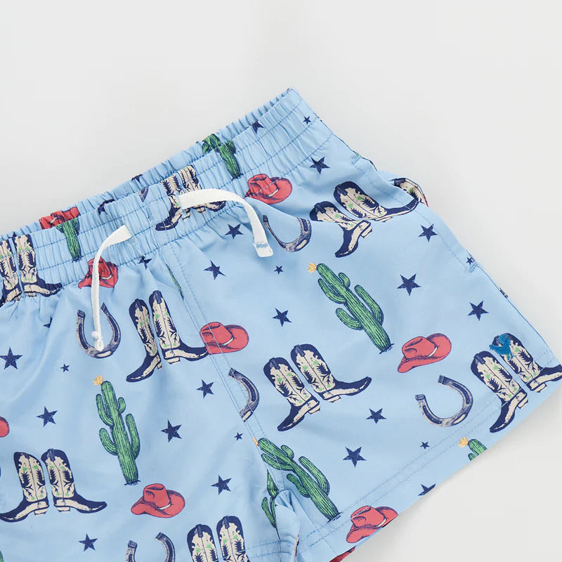 Baby boy swim trunks with blue background with images of cacti, boots, cowboy hats, horseshoes and stars all over