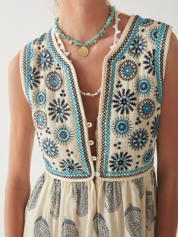 Woman wearing midi length dress with paisley print in cream and blue with vest top that buttons down and is attached to the dress
