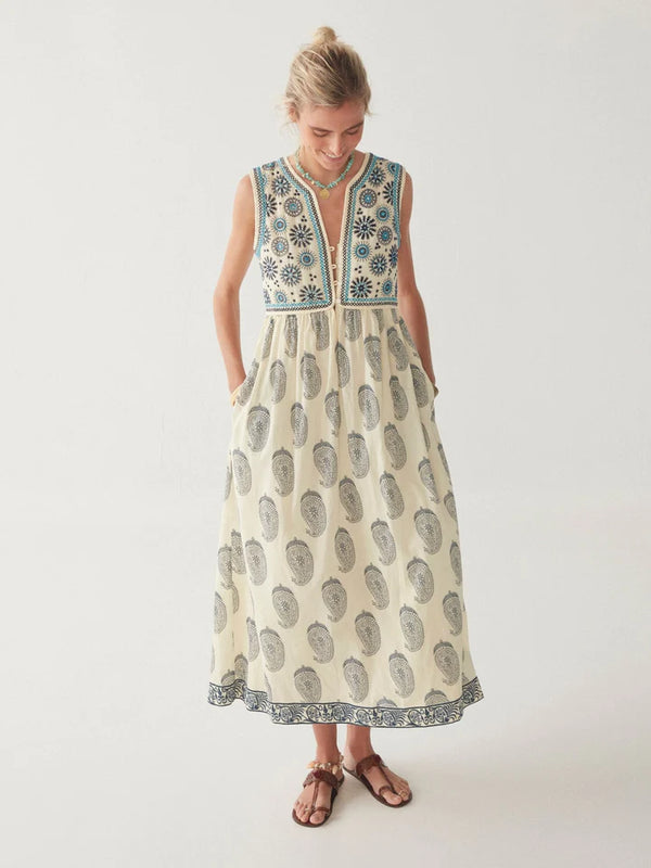 Woman wearing midi length dress with paisley print in cream and blue with vest top that buttons down and is attached to the dress