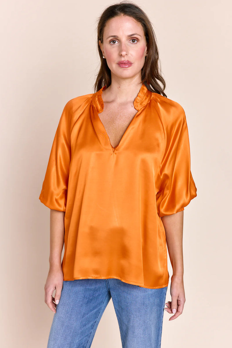 Woman wearing orange silk v neck top with dramatic collar and balloon mid sleeves