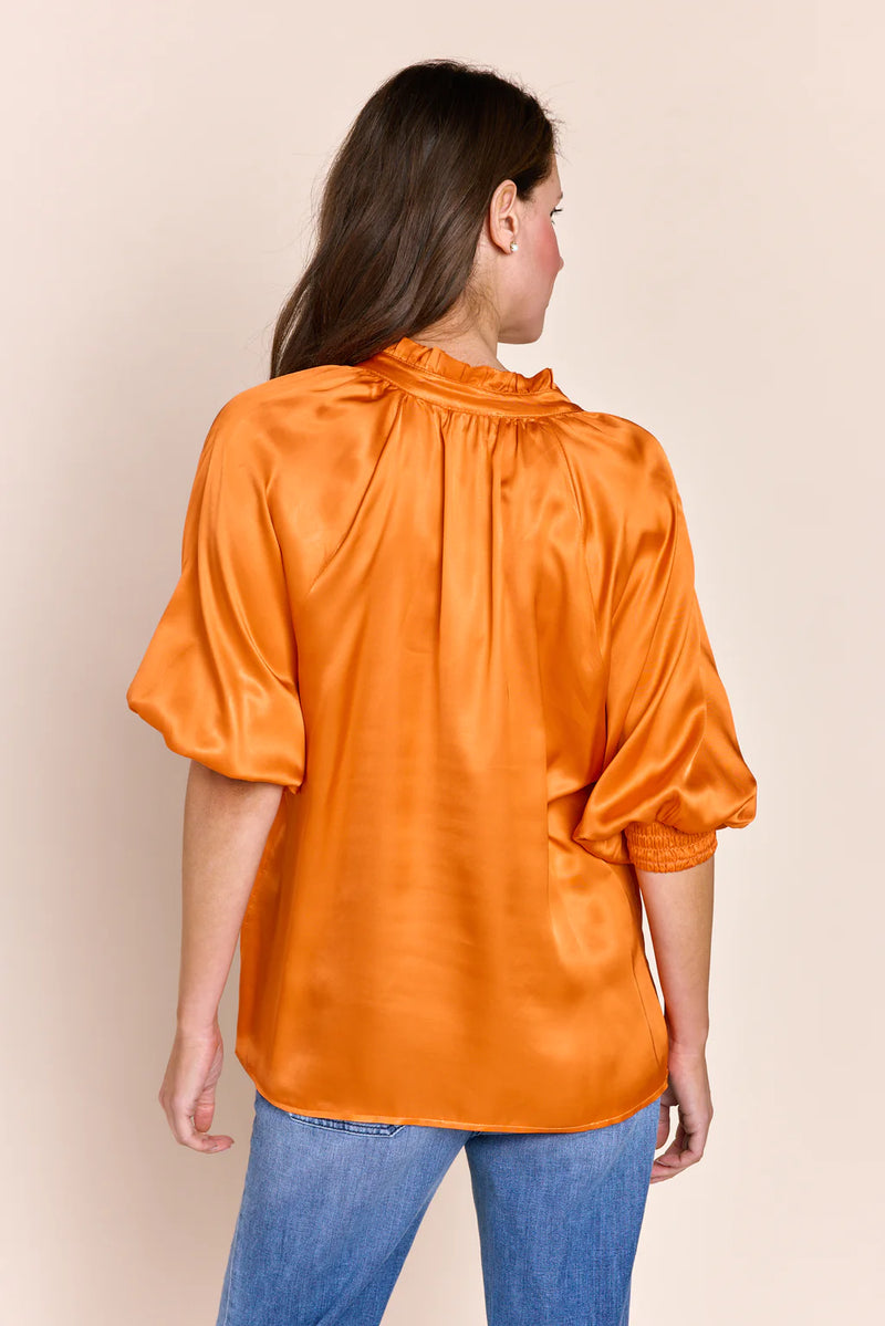 Woman wearing orange silk v neck top with dramatic collar and balloon mid sleeves