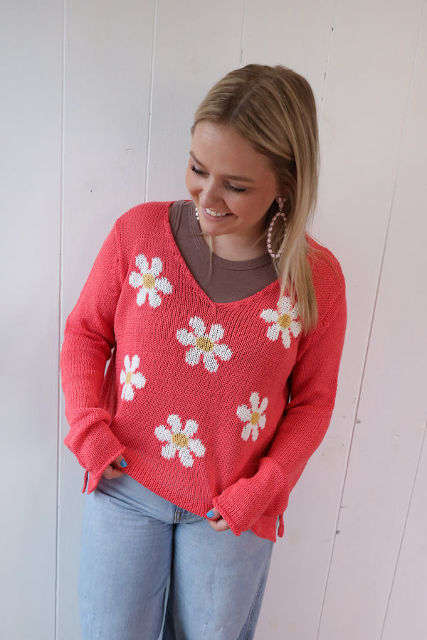 Woman wearing coral color sweater with white daisy pattern on front