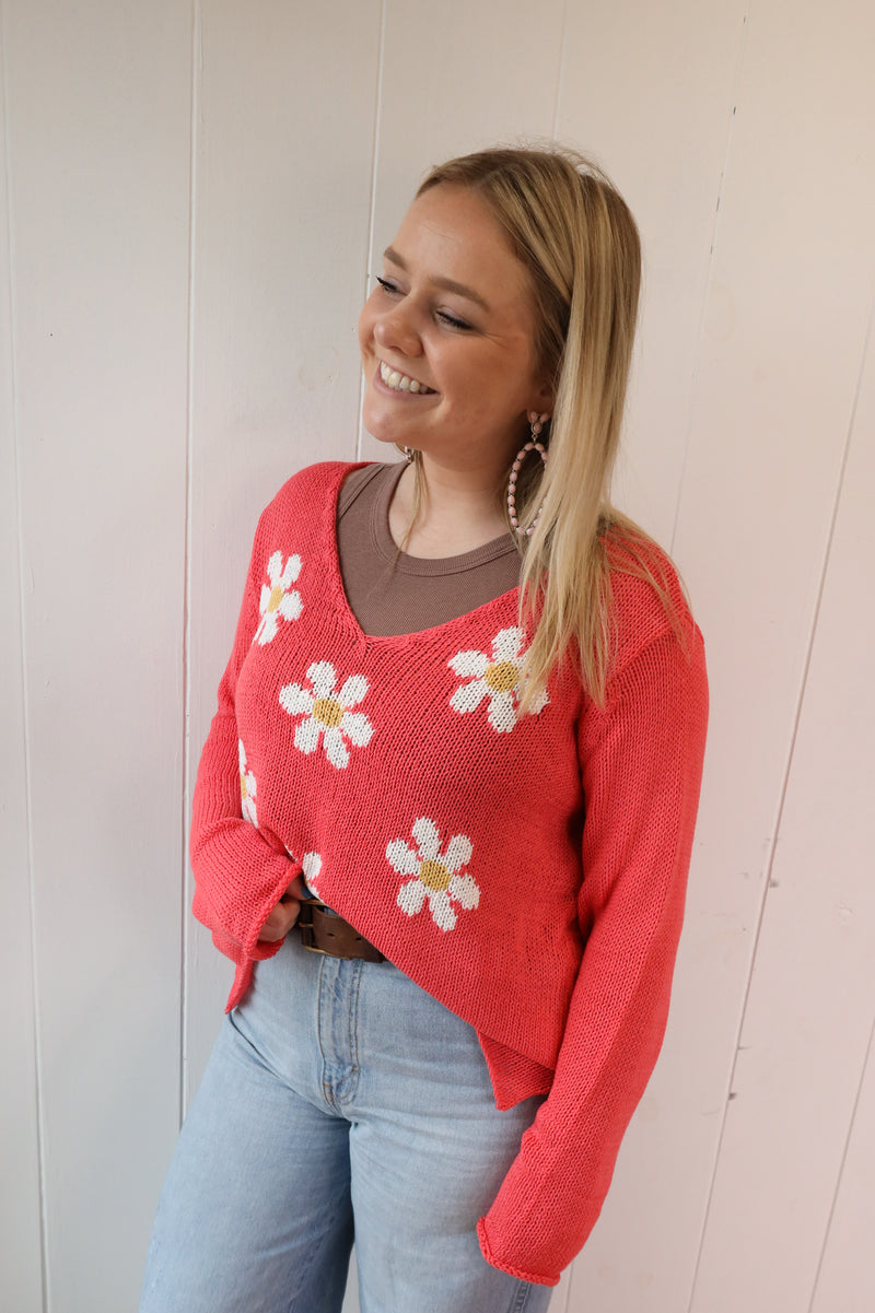 Woman wearing coral color sweater with white daisy pattern on front