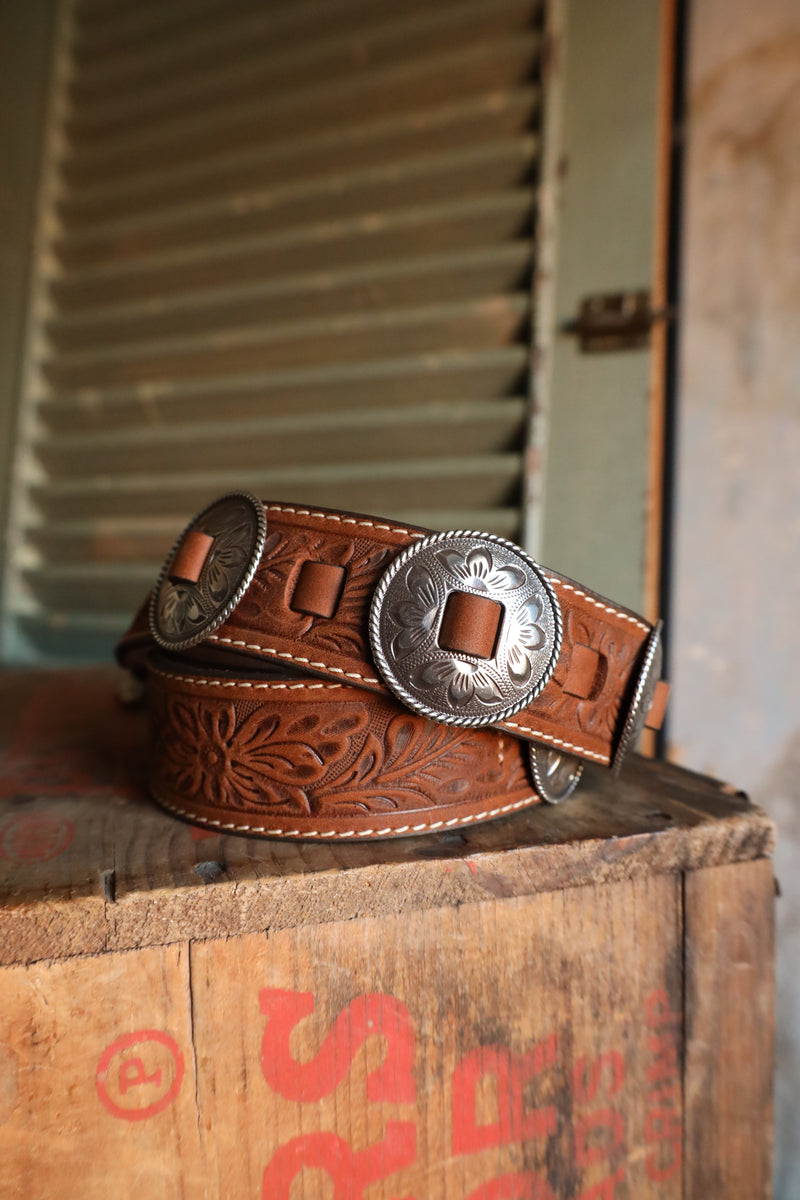 Brown tooled leather belt with silver conchos on it