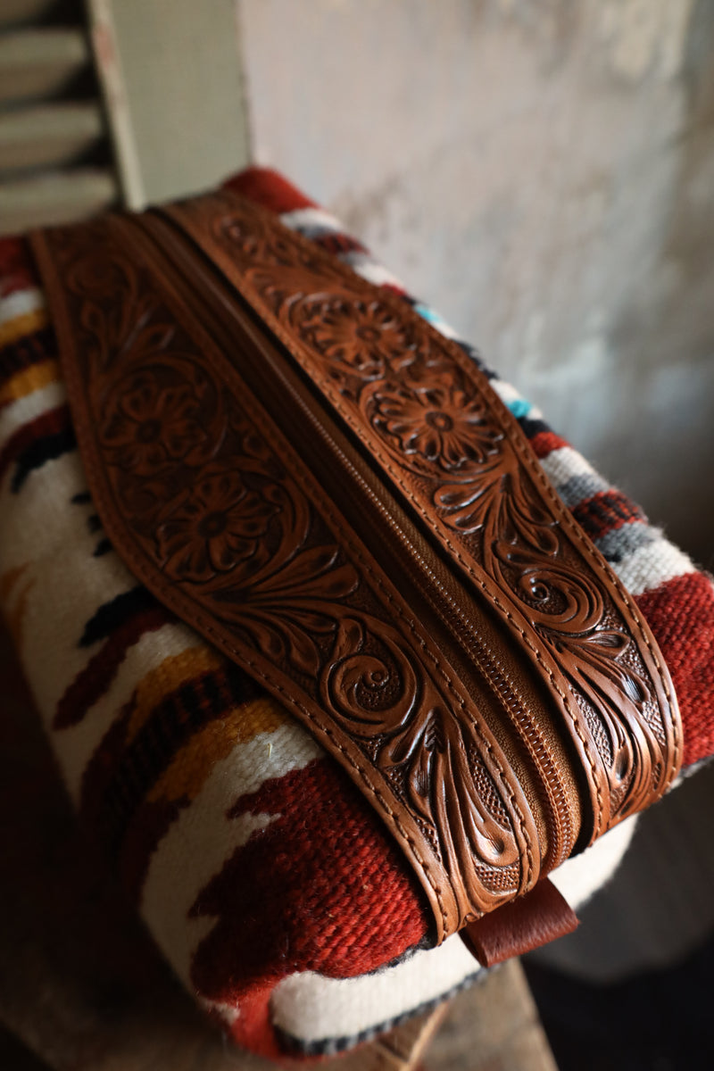 Shave kit or cosmetic bag with Aztec pattern that is embellished by tooled leather. Zipper closure and handle for easy travel