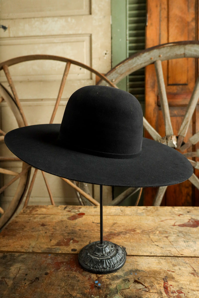 Black wide-brimmed hat on a stand with a rustic wooden background