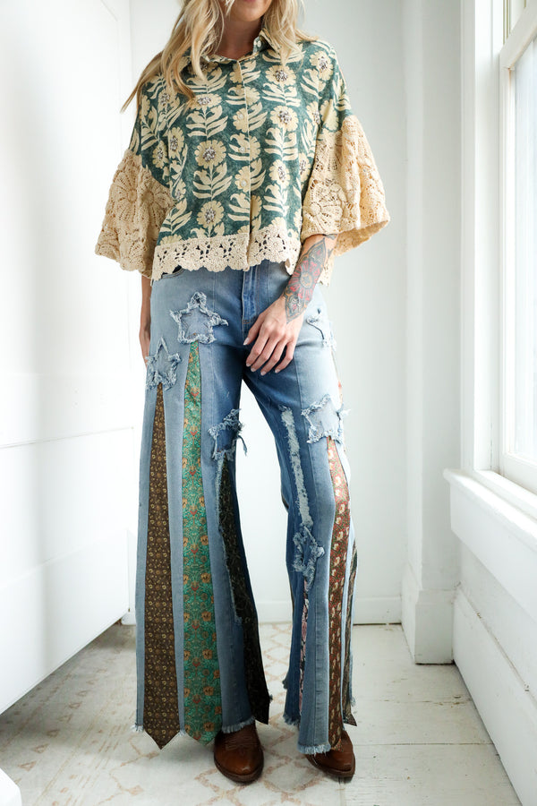 Person wearing a floral blouse and ripped jeans with a patterned ties on it in a bright room.