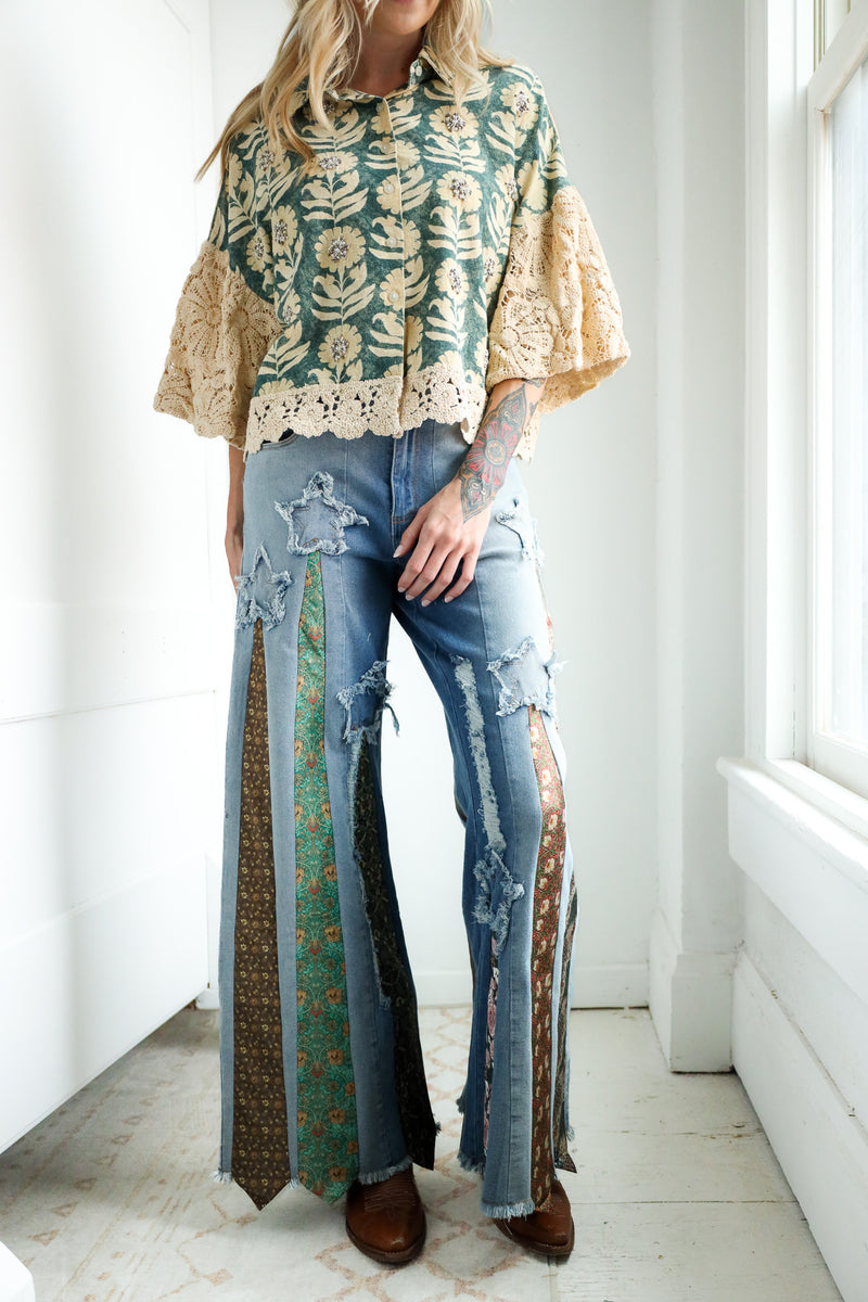 Person wearing a floral blouse and ripped jeans with a patterned ties on it in a bright room.