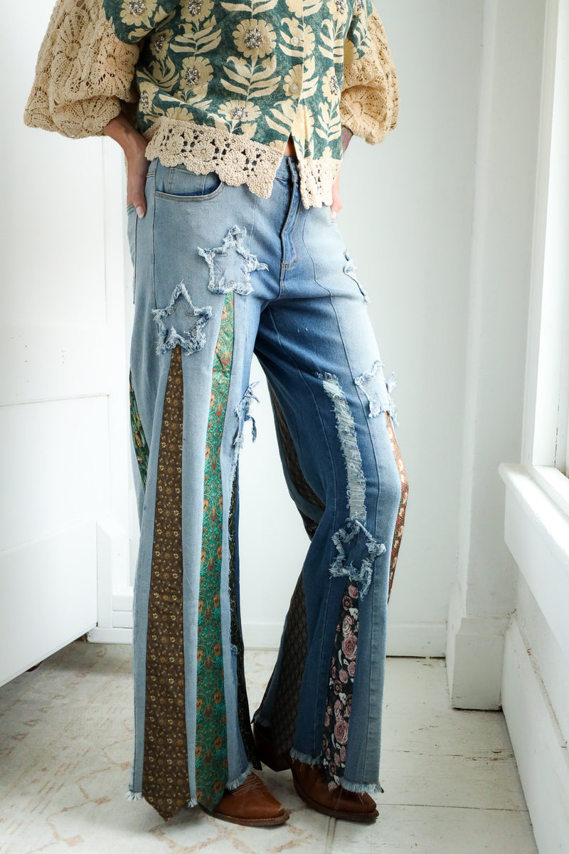 Person wearing a floral blouse and ripped jeans with a patterned ties on it in a bright room.