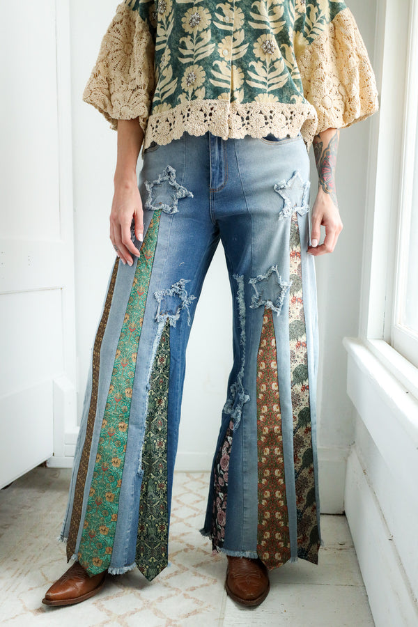 Person wearing a floral blouse and ripped jeans with a patterned ties on it in a bright room.