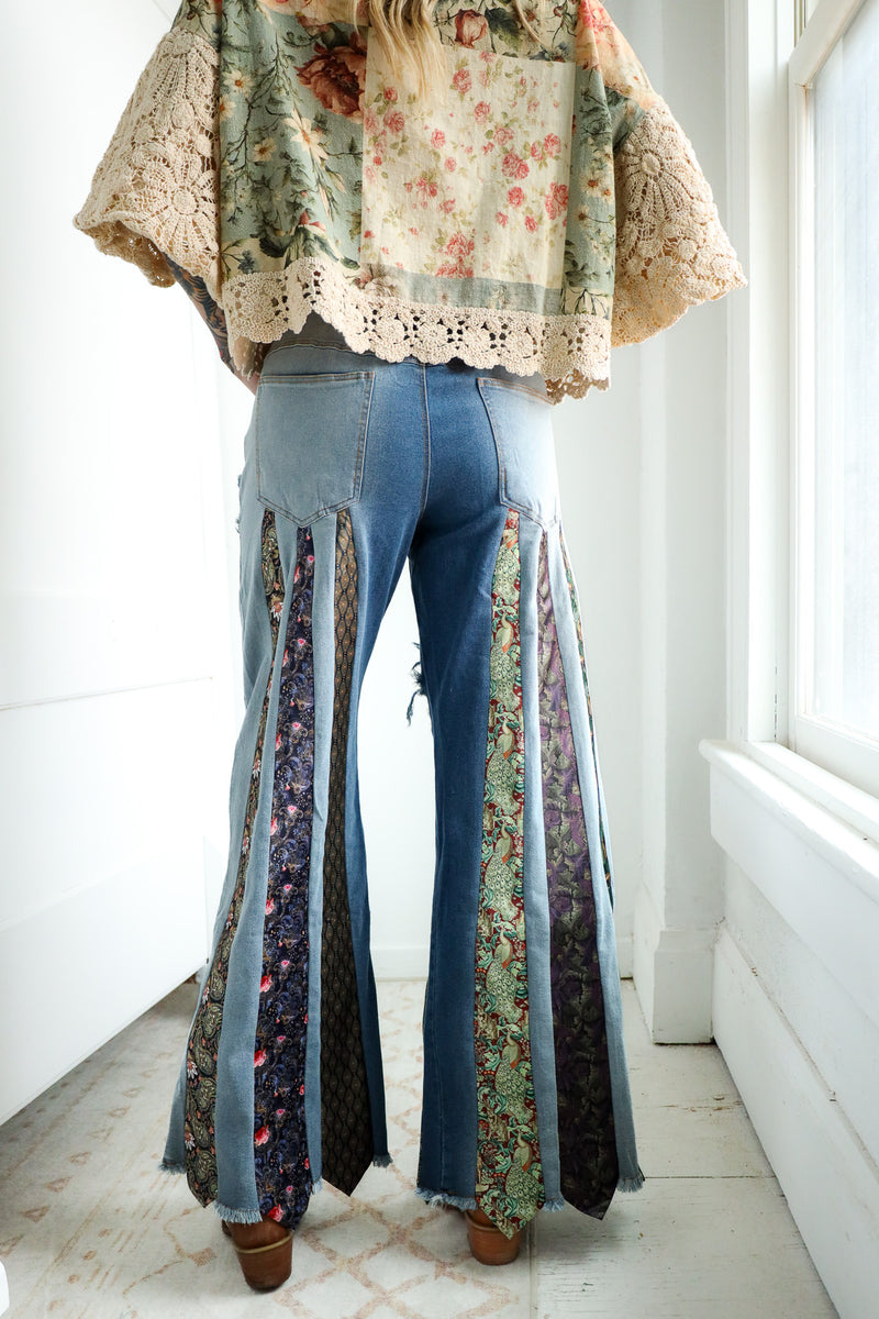 Person wearing a floral blouse and ripped jeans with a patterned ties on it in a bright room.