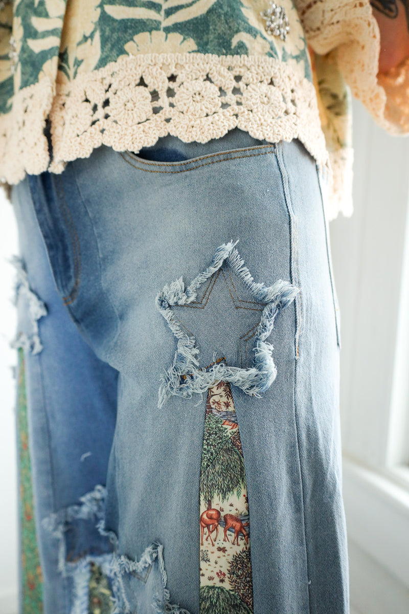 Person wearing a floral blouse and ripped jeans with a patterned ties on it in a bright room.