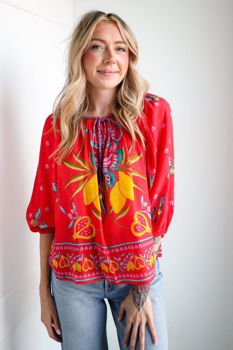 Woman wearing a red blouse with colorful floral patterns against a white background
