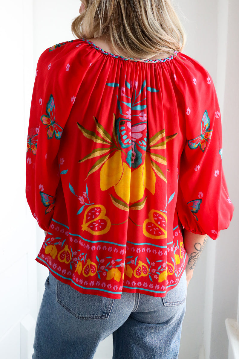 Red blouse with colorful floral and butterfly pattern worn by a person.