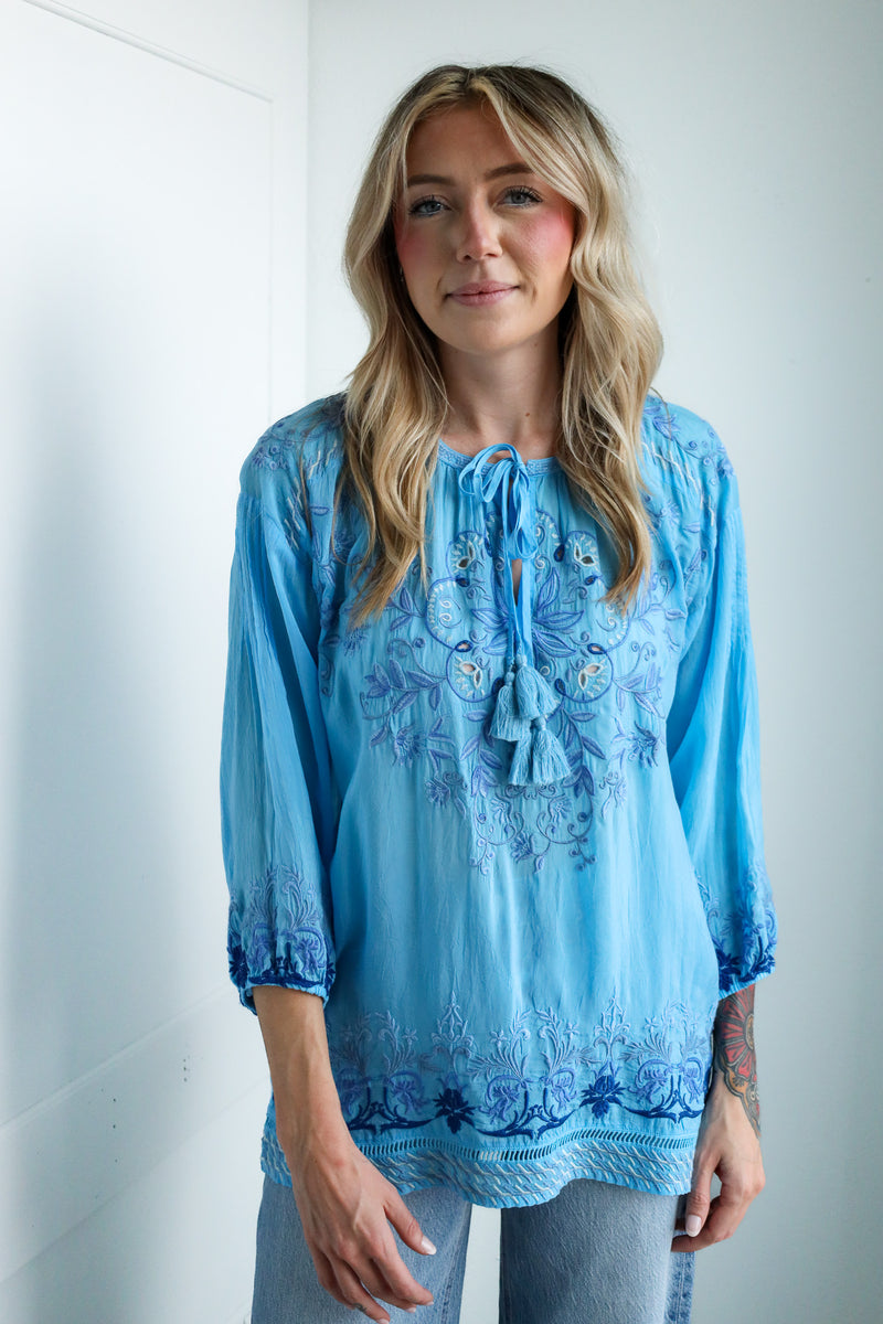 Woman wearing a blue embroidered blouse against a white background