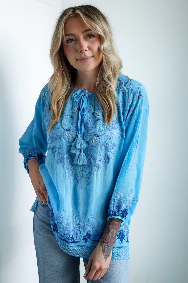Woman wearing a blue embroidered blouse against a white background