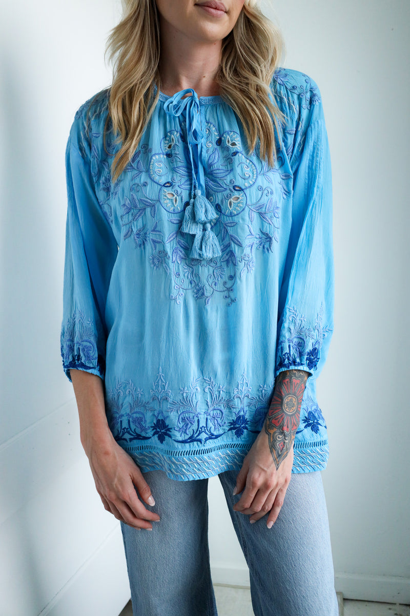 Woman wearing a blue embroidered blouse against a white background