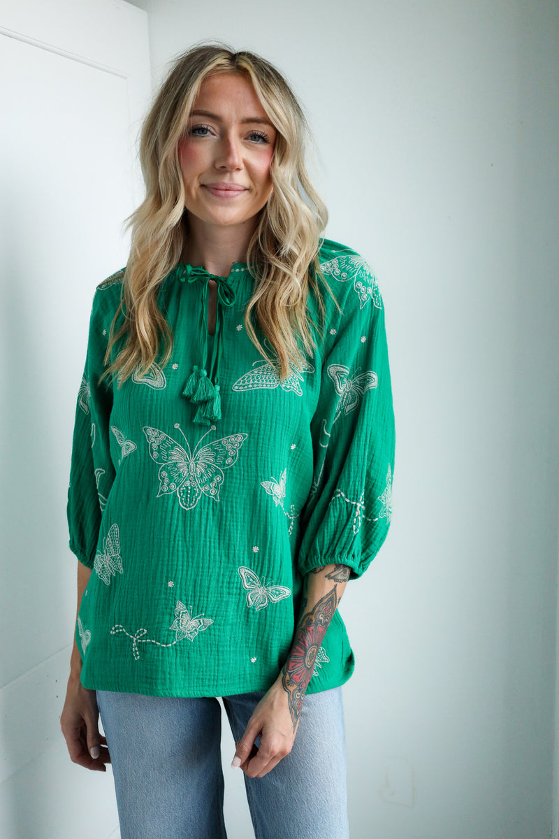 Woman wearing a green blouse with butterfly patterns against a white background