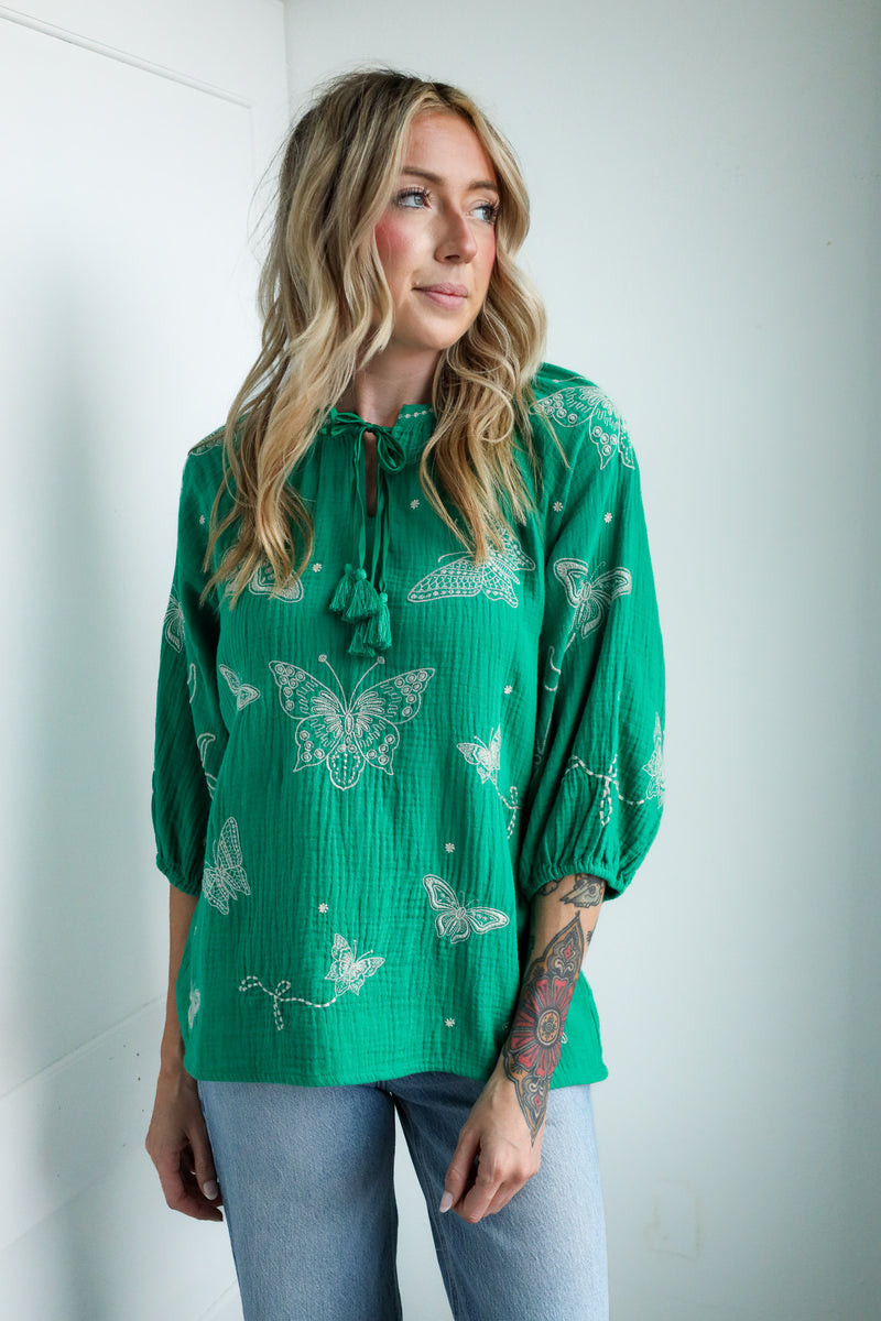 Woman wearing a green blouse with butterfly patterns against a white background