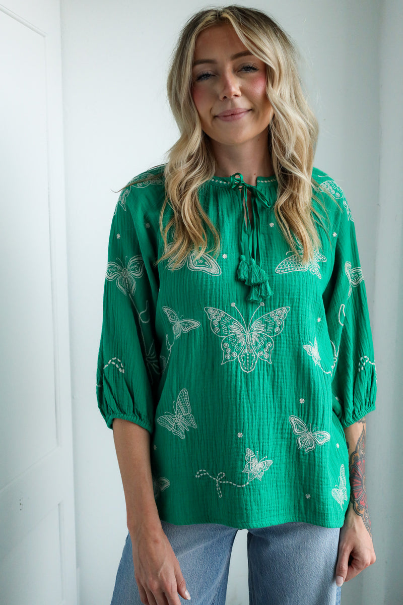 Woman wearing a green blouse with butterfly patterns against a white background
