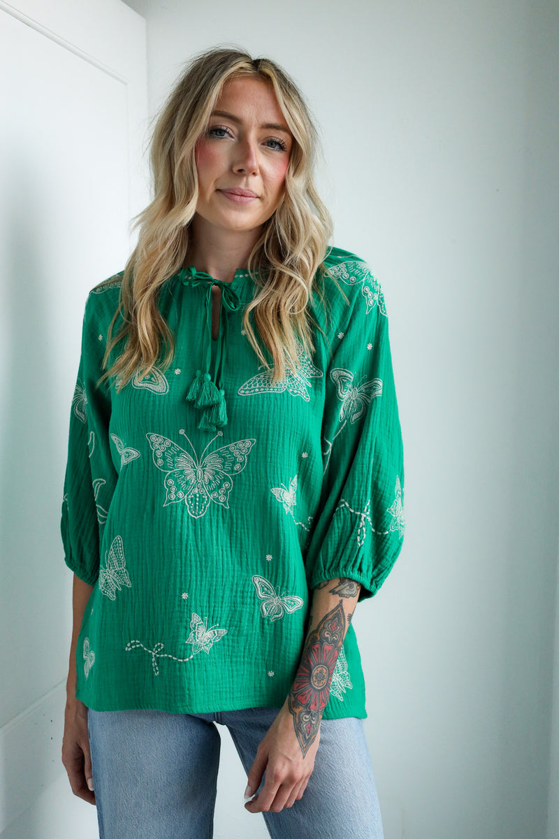 Woman wearing a green blouse with butterfly patterns against a white background