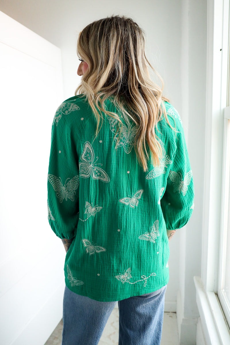 Person wearing a green blouse with butterfly patterns in a bright room.