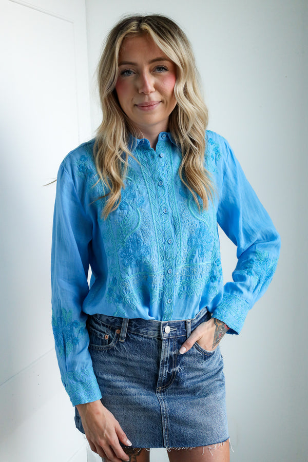 Woman wearing a blue lace blouse and denim skirt against a white background