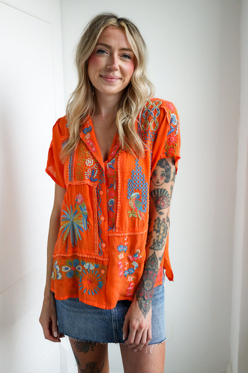 Woman wearing an orange embroidered top with a plain background