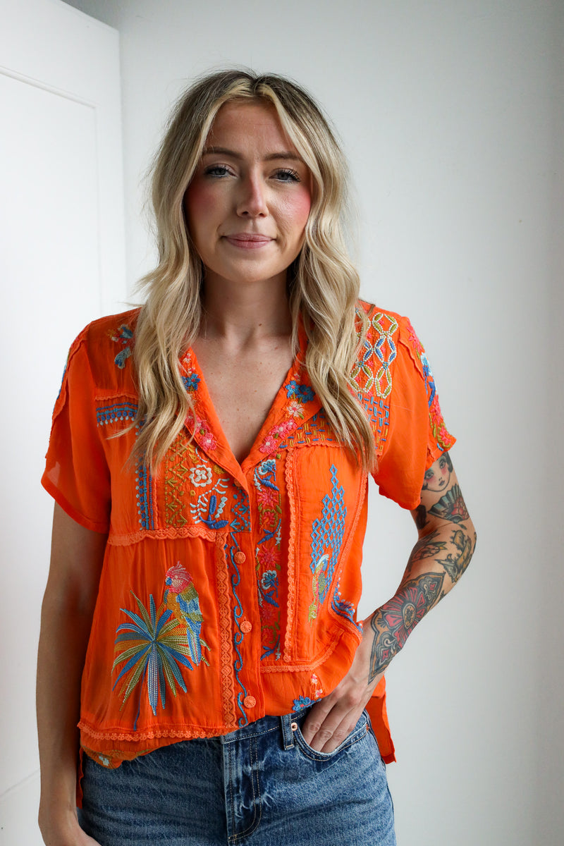 Woman wearing an orange embroidered blouse with a plain background