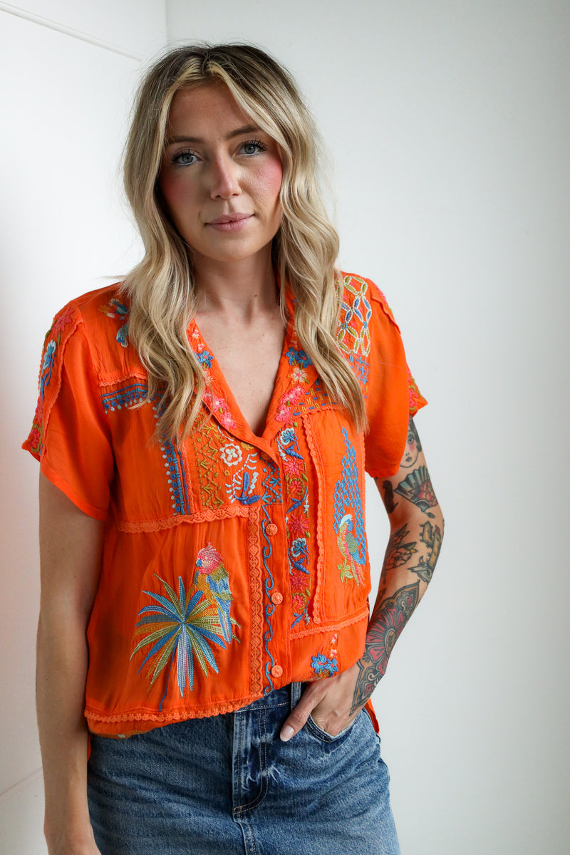 Woman wearing an orange embroidered blouse with a white background